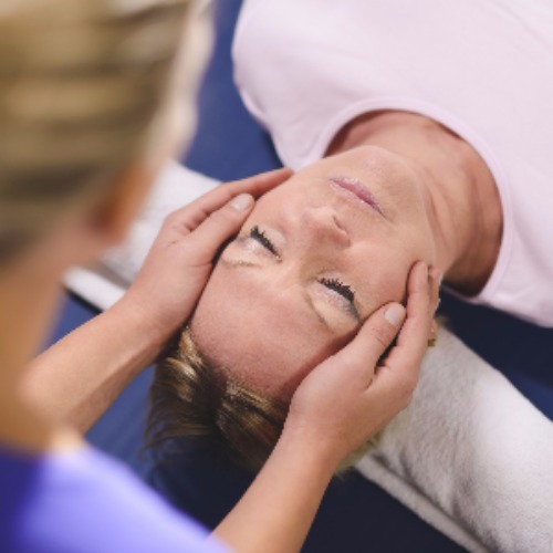 Woman receiving reiki treatment, with therapists hands on either side of her head